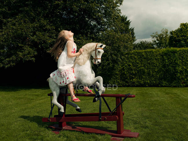 Una giovane ragazza su un cavallo a dondolo — Foto stock