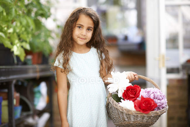 Cute girl holding basket of fresh flowers in greenhouse — Stock Photo
