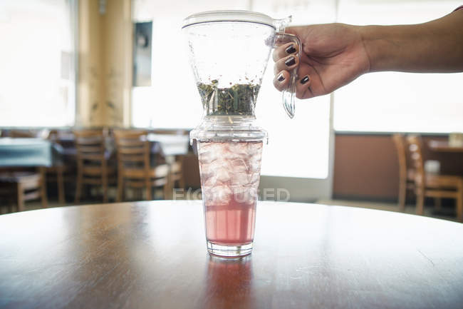 Mão feminina com chá de ervas geladas e filtro no café — Fotografia de Stock