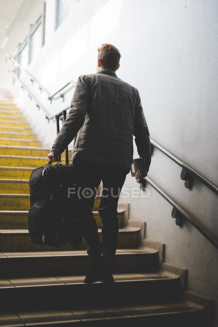 Visão traseira do jovem empresário viajante em escadas transportando mala . — Fotografia de Stock