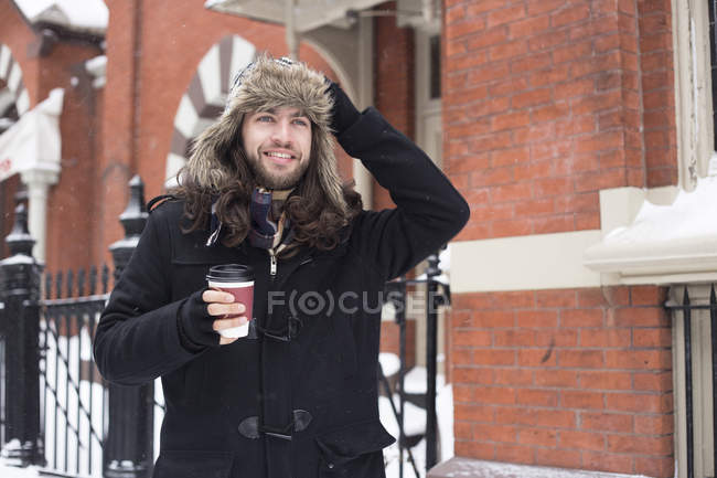 Молодой человек прогуливается по улице и пьет кофе на вынос. — стоковое фото