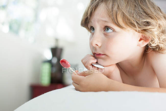 Boy holding lollipop on bed — Stock Photo