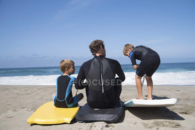 Vista posteriore del padre e due figli che si esercitano con i bodyboard sulla spiaggia, Laguna Beach, California, USA — Foto stock