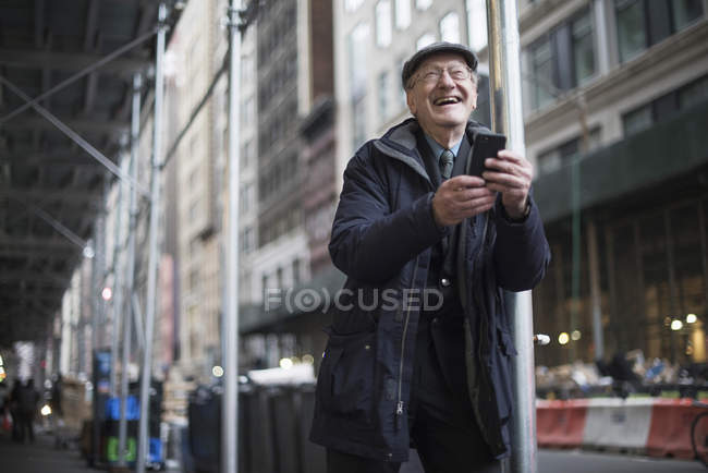 Mann lehnt an Laternenpfahl, hält Smartphone lachend, manhattan, new york, usa — Stockfoto