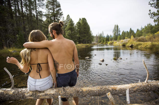 Rückansicht eines jungen Paares, das auf einem umgestürzten Baum im Fluss sitzt, Lake Tahoe, Nevada, USA — Stockfoto