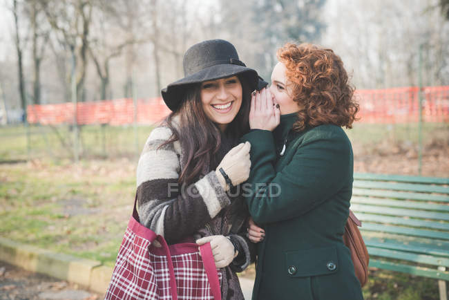 Two female adult friends whispering in park — Stock Photo
