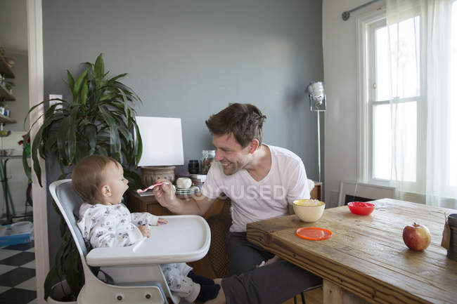 Kleiner Junge sitzt im Hochstuhl, Vater füttert ihn mit Essen — Stockfoto