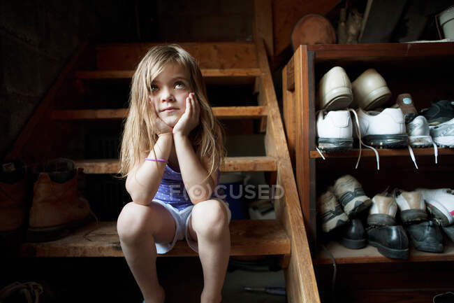 Little girl sitting on basement steps, looking up — Stock Photo