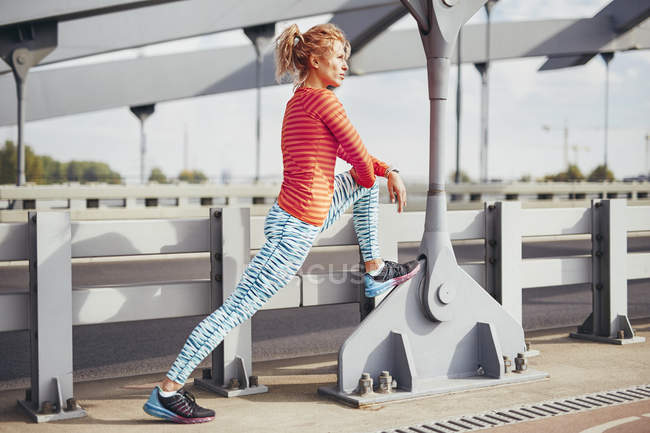 Young female runner warming up on city footbridge — Stock Photo