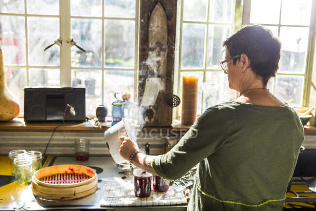 Вид сзади женщины, наливающей свеклу в консервные банки на кухне — стоковое фото