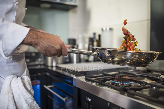 Шеф-повар держит сковородку, готовит еду над плитой, крупным планом — стоковое фото