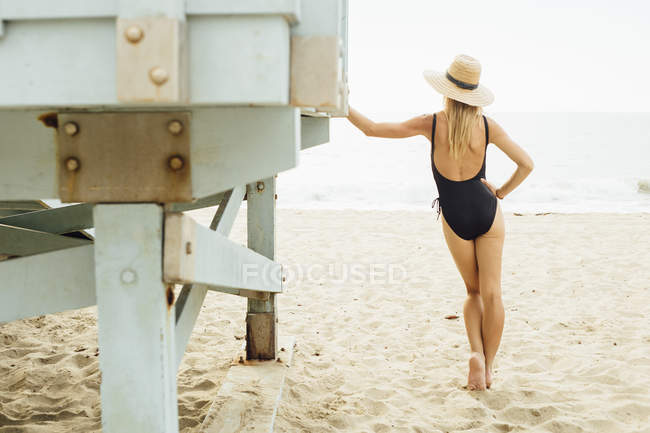 Rear view of woman wearing swimsuit leaning against lifeguard tower — Stock Photo