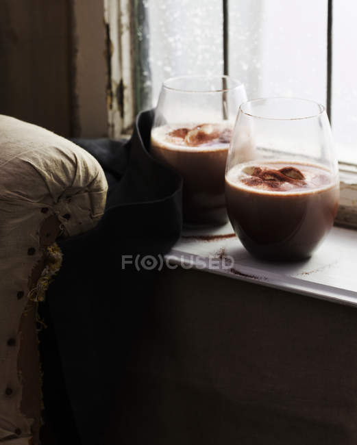 Glasses of hot chocolate on windowsill — Stock Photo