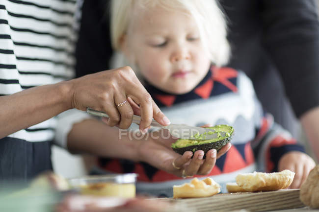 Cropped image of woman preparing avocado for boy — Stock Photo