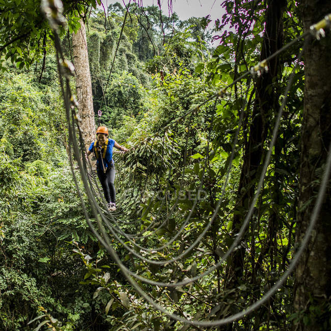 Женщина, пересекающая веревочный мост в лесу, Пан Нонглуанг, провинция Чампассак, Паксонг, Лаос — стоковое фото