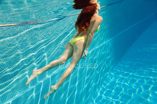 Mujer joven nadando bajo el agua en la piscina - foto de stock