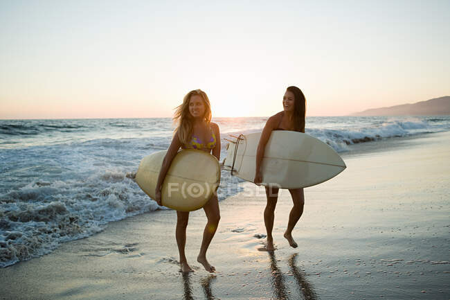 Женщины-серферы на берегу моря на закате — стоковое фото
