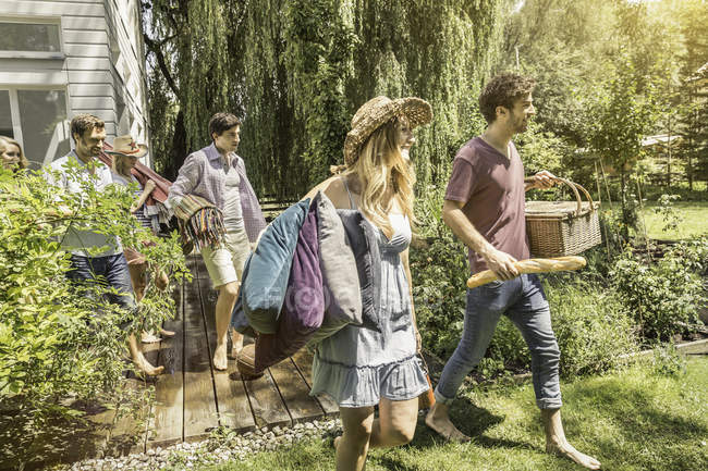 Amigos masculinos y femeninos caminando en el jardín preparándose para el picnic - foto de stock