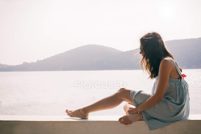 Jovem mulher sentada na parede por mar, Ilha Burgaz, Istambul, Turquia — Fotografia de Stock