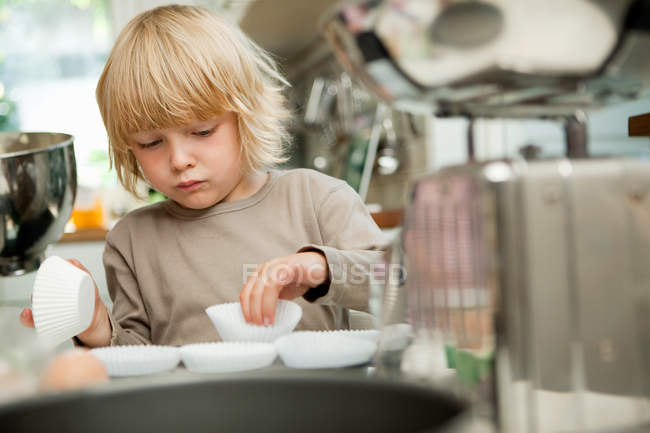 Boy arranging cake cases on baking tray — Stock Photo