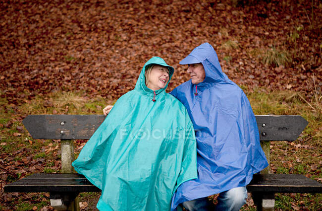 Senior couple sitting on park bench wearing waterproofs — Stock Photo
