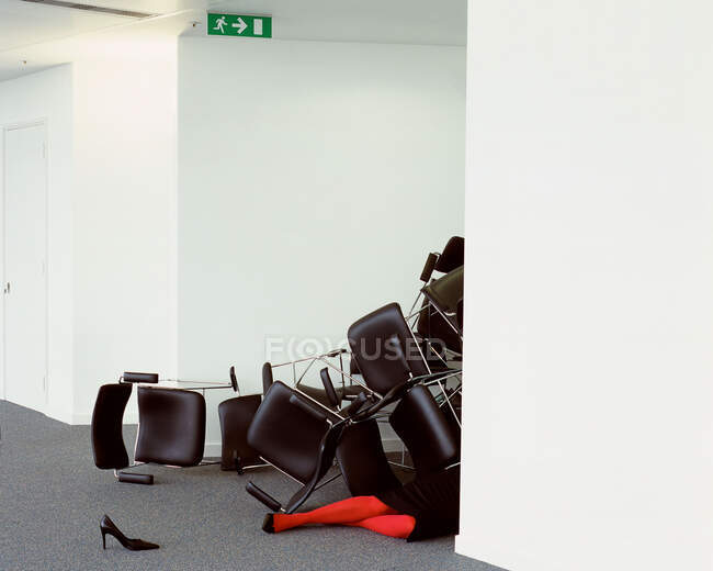 Mujer de negocios atrapada debajo de una pila de sillas - foto de stock
