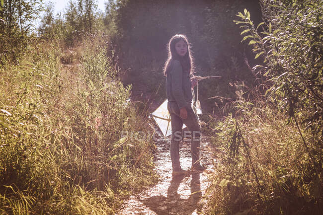 Дівчина-підліток тримає повітряний змій, озираючись назад від брудної доріжки — стокове фото