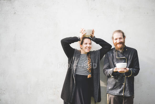 Couple standing in front of wall holding pots looking at camera smiling — Stock Photo