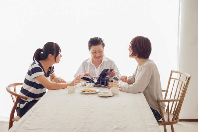 Familia de tres generaciones mirando álbum de fotografía - foto de stock