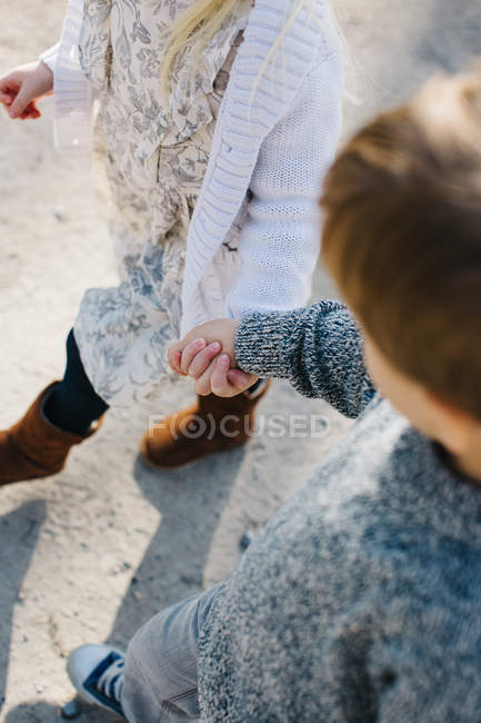 Image recadrée de frères et sœurs tenant la main marchant sur un chemin de gravier — Photo de stock