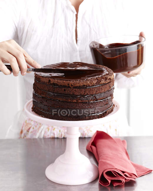 Cropped image of woman icing chocolate layer cake — Stock Photo