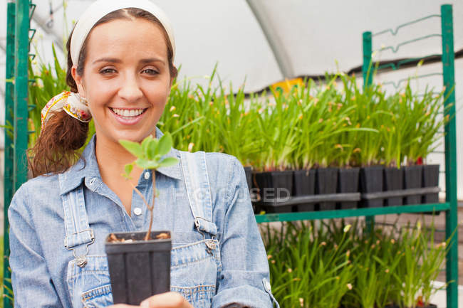 Young woman holding plant in garden centre, portrait — Stock Photo
