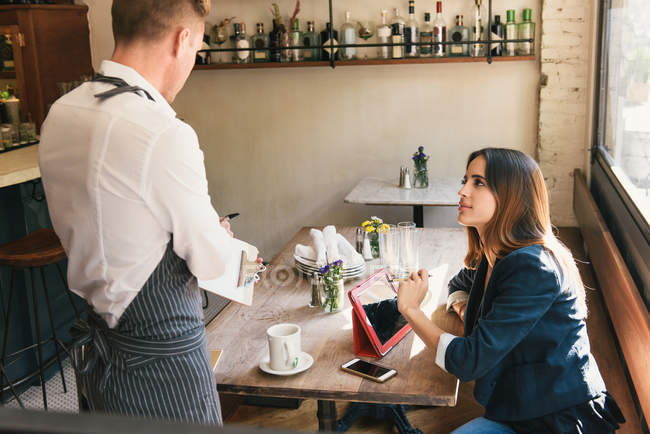 Официант и молодая женщина обсуждают меню в ресторане — стоковое фото
