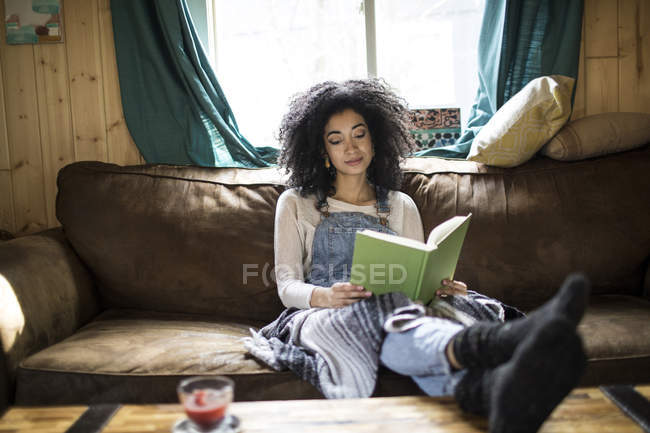 Young woman sitting on sofa, reading book — Stock Photo