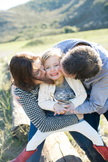 Casal adulto meados beijando bochechas da filha no campo — Fotografia de Stock