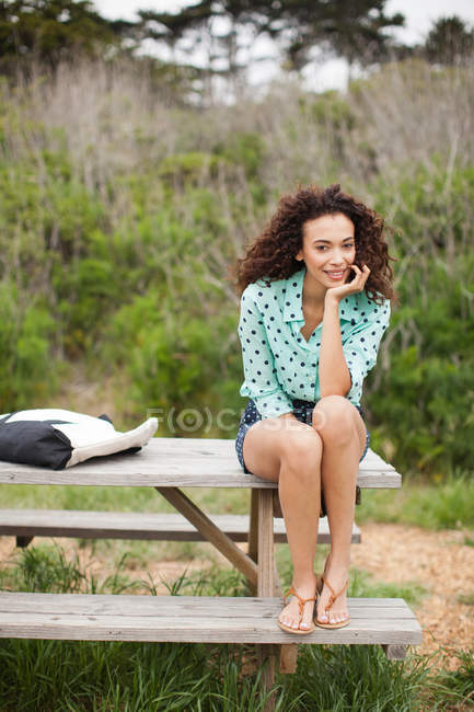 Молода жінка сидить на столі пікніка посміхається, портрет — стокове фото