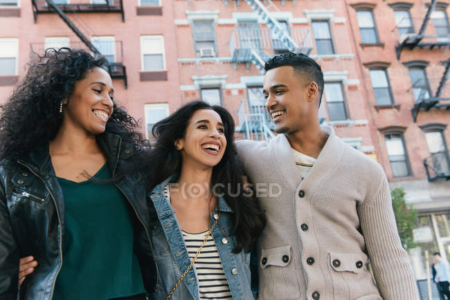Tres amigos adultos con brazos alrededor en la calle de la ciudad - foto de stock