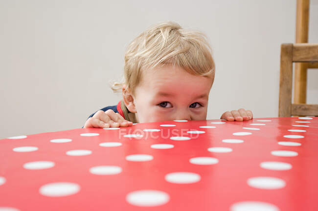Niño mirando por encima de la mesa - foto de stock