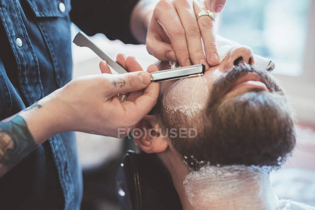 Barbier rasage visage client avec rasoir droit — Photo de stock