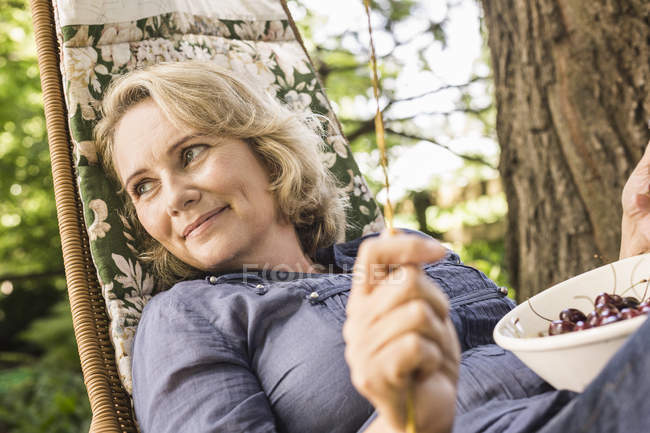 Reife Frau entspannt sich mit Schüssel Kirschen auf Hängematte — Stockfoto
