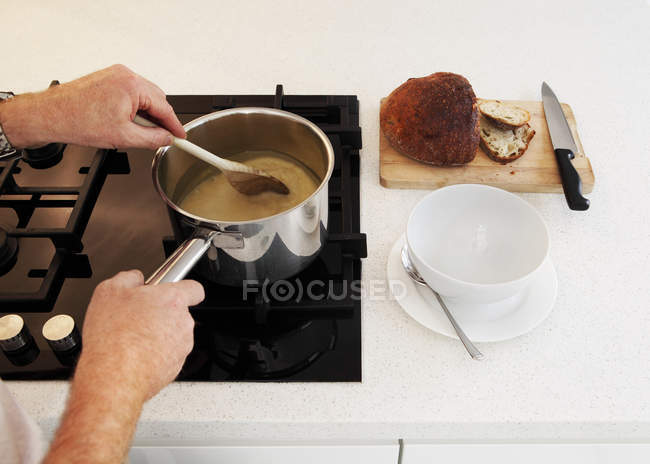 Hombre revolviendo cacerola de sopa en la encimera - foto de stock