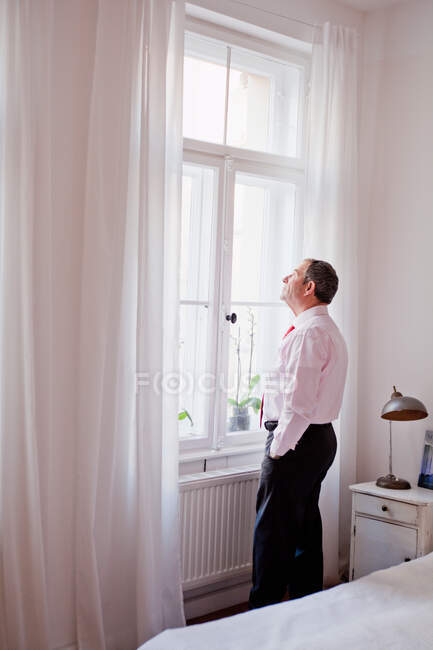 Hombre pensativo de pie frente a la ventana - foto de stock