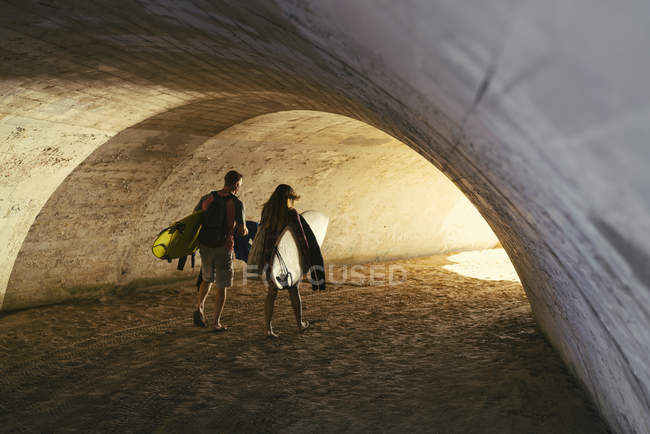 Rear view of surfing couple walking through beach underpass, Newport Beach, California, USA — Stock Photo