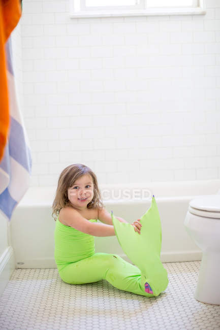 Portrait of girl in lime green mermaid costume sitting on bathroom floor — Stock Photo