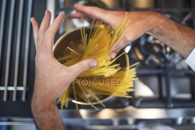 Chef putting spaghetti in saucepan on stove, close-up, overhead view — Stock Photo