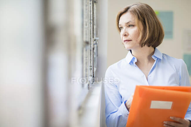 Зріла бізнес-леді з файлом дивиться з офісного вікна — стокове фото