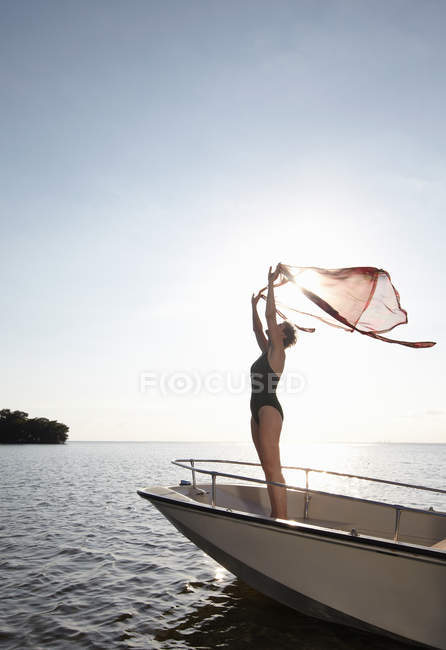Senior woman holding sarong mid air on motorboat — Stock Photo
