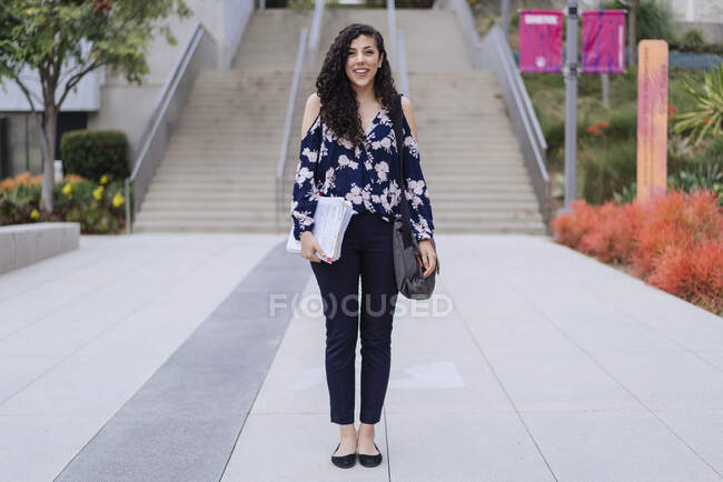 Porträt einer jungen Frau, die im Freien steht, Tasche und Papiere in der Hand hält — Stockfoto