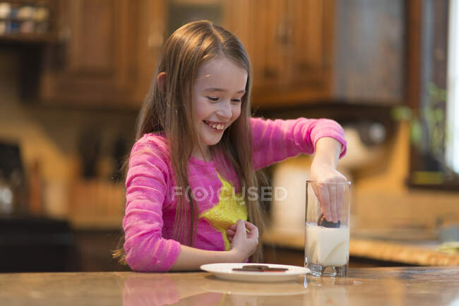 Молодая девушка с молоком и печеньем за кухонным столом — стоковое фото