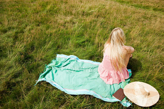 Young woman sitting on a scarf in a field — Stock Photo